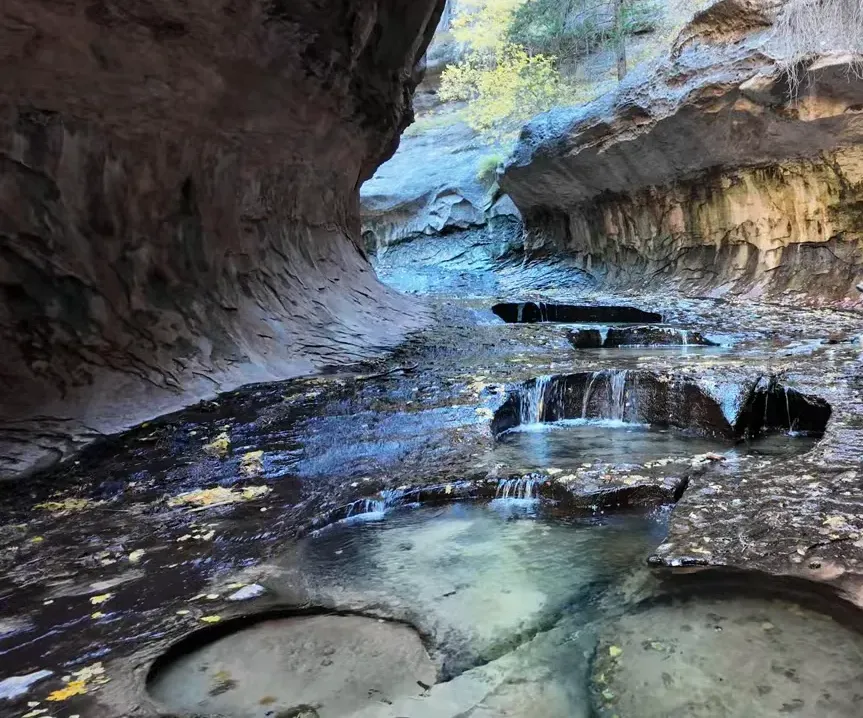 Panoramic view of the Subway slot canyon approach with carved pools and a hiker near the right wall