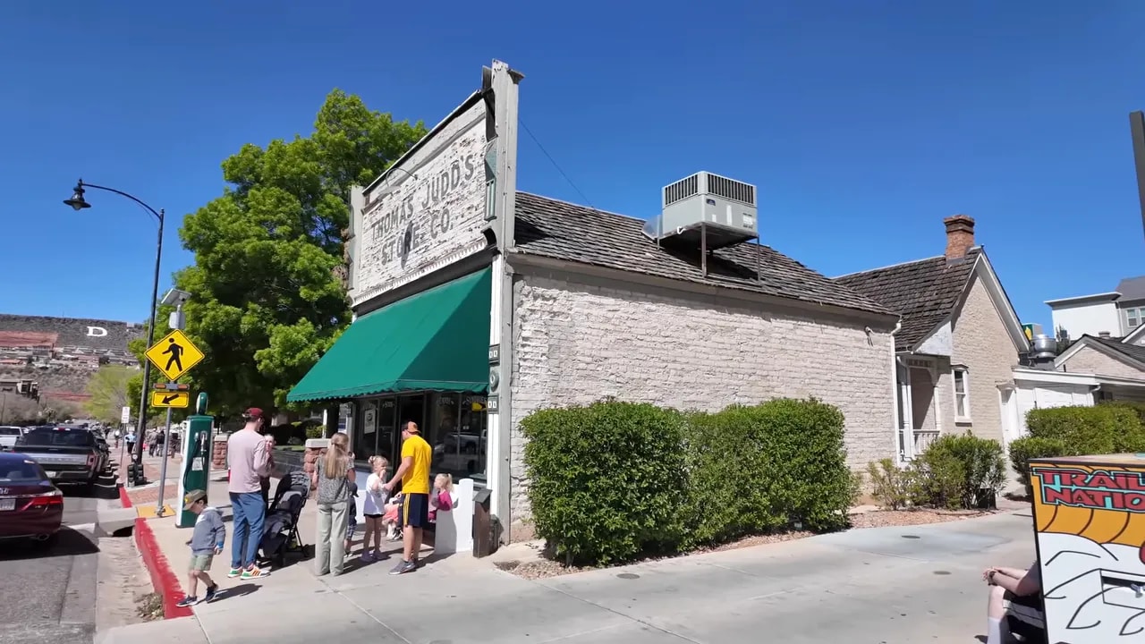 Wide-angle view of downtown St. George showing a historic storefront with green awning, people on the sidewalk and parked cars.