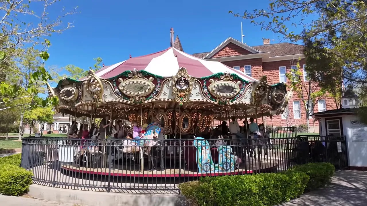 Wide view of an ornate carousel at Green Gate Village with a red-brick historic building behind it